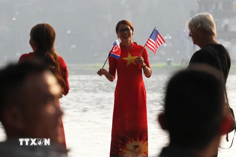 Thiếu nữ mặc áo dài in Quốc kỳ Việt Nam, cầm cờ Mỹ và Triều Tiên chào mừng Hội nghị ở khu vực hồ Hoàn Kiếm. (Ảnh: Lâm Khánh/TTXVN)
