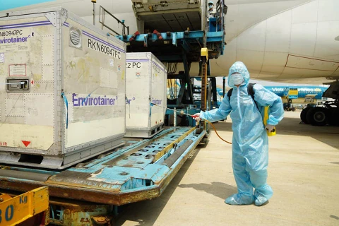 Nhân viên làm công tác khử khuẩn các lô hàng gồm 117.600 liều vắcxin phòng COVID-19 đầu tiên về Việt Nam. (Ảnh: PV/Vietnam+)