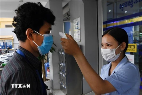 Nhân viên y tế kiểm tra thân nhiệt một khách hàng nhằm ngăn dịch COVID-19 lây lan, bên ngoài một ngân hàng ở Phnom Penh, Campuchia, ngày 17/3/2020. (Ảnh: AFP/TTXVN)