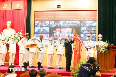 Chủ tịch nước Nguyễn Xuân Phúc gắn Huân chương Bảo vệ Tổ quốc hạng Nhất lên lá cờ truyền thống của lực lượng an ninh nhân dân. (Ảnh: Phạm Kiên/TTXVN)