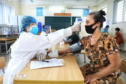 Nhân viên y tế kiểm tra nhiệt độ và huyết áp cho người dân trước khi tiêm vaccine phòng COVID-19. (Ảnh: Thành Đạt/TTXVN)