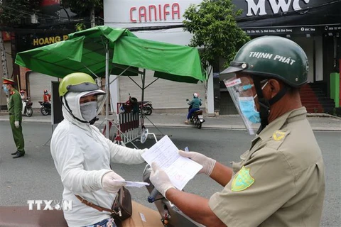 Một người phụ nữ đi chợ trình giấy có giấy tiêm đủ vaccine cho lực lượng kiểm tra trên đường Yersin, thành phố Thủ Dầu Một. (Ảnh: Chí Tưởng/TTXVN)