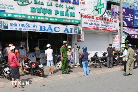 Lực lượng công an nhắc nhở người dân giữ khoảng cách an toàn khi mua hàng hóa, tại thị trấn Bến Lức, huyện Bến Lức, tỉnh Long An. (Ảnh: Thanh Bình/TTXVN)