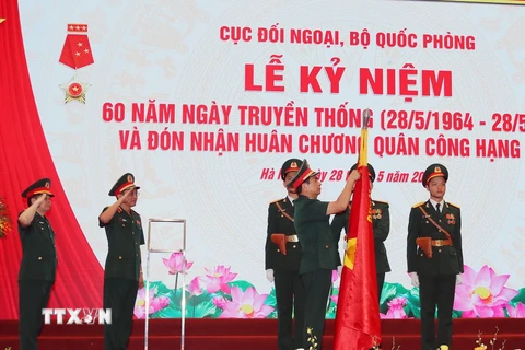 Đại tướng Phan Văn Giang, Ủy viên Bộ Chính trị, Phó Bí thư Quân ủy Trung ương, Bộ trưởng Bộ Quốc phòng gắn Huân chương Quân công hạng Nhất lên cờ truyền thống của Cục Đối ngoại. (Ảnh: Trọng Đức/TTXVN)