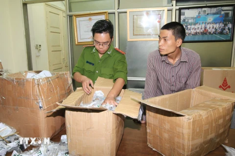 Cảnh sát kiểm tra số hàng giả của đối tượng Đỗ Văn Đạt. (Ảnh: Doãn Tấn/TTXVN)