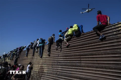 Người di cư vượt qua hàng rào biên giới giữa Mỹ và Mexico, gần cửa khẩu El Chaparral ở Tijuana, bang Baja California, Mexico ngày 25/11/2018. (Ảnh: AFP/TTXVN)