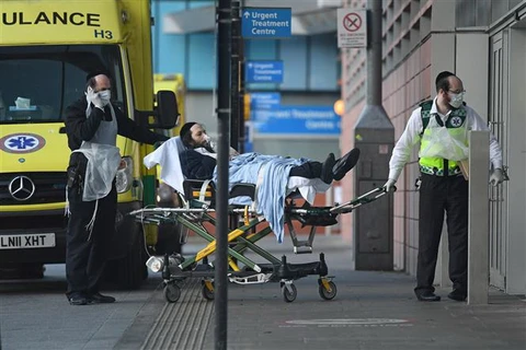 Nhân viên y tế chuyển bệnh nhân nhiễm COVID-19 tới bệnh viện ở London, Anh. (Ảnh: AFP/TTXVN)