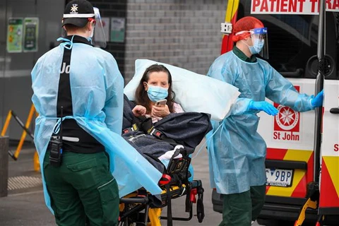 Nhân viên y tế chuyển bệnh nhân mắc COVID-19 lên xe cứu thương tại bang Victoria, Australia(Ảnh: AFP/TTXVN)