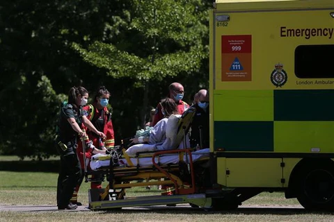Nhân viên y tế chuyển bệnh nhân mắc COVID-19 lên xe cứu thương tại London, Anh. (Ảnh: AFP/TTXVN)