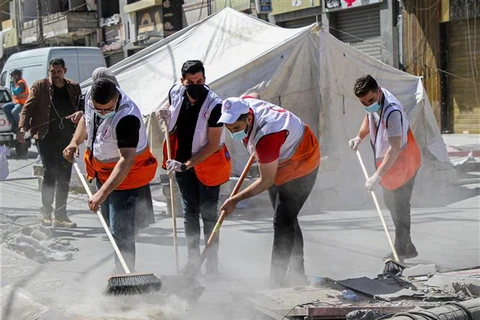 Các tình nguyện viên dọn dẹp đống đổ nát của các tòa nhà bị sập sau loạt không kích của Israel xuống Dải Gaza. (Ảnh: THX/TTXVN)
