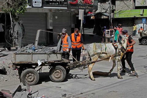 Các tình nguyện viên dọn dẹp đống đổ nát của các tòa nhà bị sập sau loạt không kích của Israel tại Dải Gaza. (Ảnh: AFP/TTXVN)