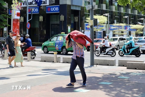 Một người dân tại Thành phố Hồ Chí Minh dùng áo che kín đầu, bước vội giữa trời nắng nóng. (Ảnh: Hồng Giang/TTXVN)