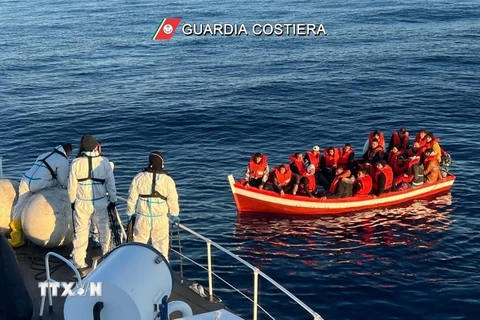 Tàu của lực lượng bảo vệ bờ biển Italy tiếp cận thuyền chở người di cư trong chiến dịch giải cứu ngoài khơi Italy. (Ảnh: AFP/TTXVN)