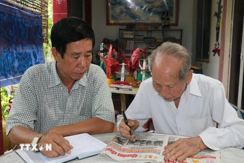 Ông Nguyễn Văn Thọ (phải) và con trai Nguyễn Thanh Hà đọc thông tin ở mục tìm thân nhân liệt sỹ trên báo. (Ảnh: Hữu Chí/TTXVN)