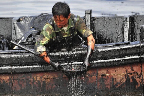 Một công nhân múc dầu ở cảng Đại Liên, Liêu Ninh (Trung Quốc) do vỡ đường ống dẫn dầu, khiến 1.500 tấn dầu thô tràn vào nước. (Nguồn: Techinsider)