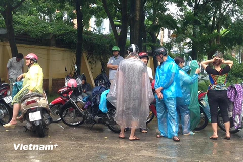 Do sân trước điểm thi của Trung tâm giáo dục thường xuyên Thanh Trì không có mái che, nên tất cả các phụ huynh đều phải mặc áo mưa. (Ảnh: Sơn Bách/Vietnam+)
