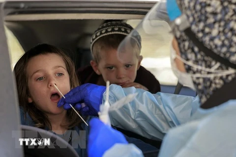 Nhân viên y tế lấy mẫu xét nghiệm COVID-19 cho một em nhỏ tại Berlin. (Ảnh: AFP/TTXVN)