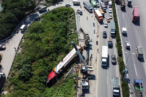 Chiếc xe container bị lật trên đường lên cầu Thanh Trì đã húc đổ cột biển báo, kéo đổ nghiêng cột khung biển báo hiệu, gây ùn tắc giao thông. (Ảnh: Huy Hùng/TTXVN) 