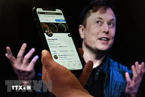 Tài khoản Twitter của tỷ phú Elon Musk trên màn hình điện thoại và ảnh chụp ông Musk (phía sau) . (Ảnh: AFP/TTXVN)