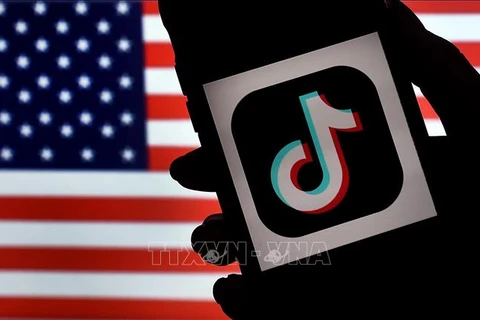 Biểu tượng ứng dụng TikTok trên màn hình điện thoại và quốc kỳ Mỹ (phía sau). (Ảnh: AFP/TTXVN)