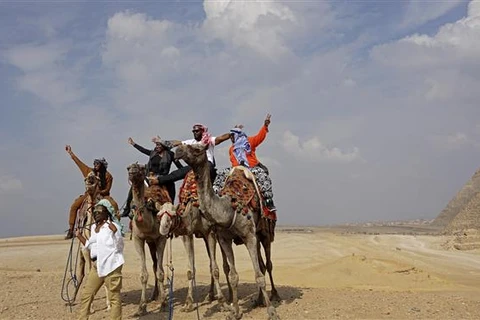 Khách du lịch cưỡi lạc đà khi tham quan quần thể Kim tự tháp Giza ở ngoại ô Cairo (Ai Cập). (Ảnh: AFP/TTXVN)