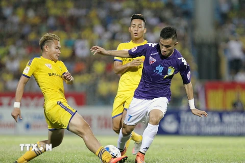 Pha tranh bóng giữa cầu thủ Sông Lam Nghệ An (áo vàng) và T&T Hà Nội (áo tím). (Ảnh: Quốc Khánh/TTXVN)