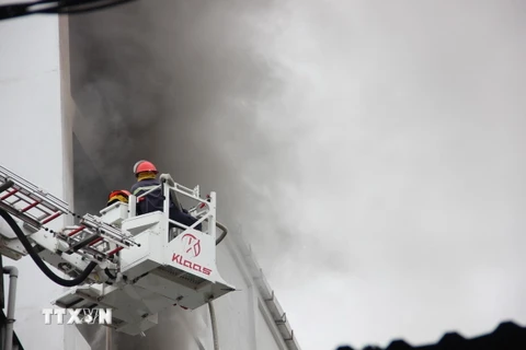 Lực lượng chữa cháy dùng xe thang tiếp cận hiện trường phun nước dập lửa. (Ảnh: Hoàng Ngà/TTXVN)