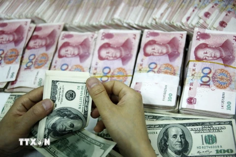 Ảnh tư liệu: Đồng tiền giấy 100 đôla Mỹ (trên) và đồng 100 Nhân dân tệ (phía dưới) tại một ngân hàng ở Hoài Bắc, tỉnh An Huy. (Nguồn: AFP/ TTXVN)