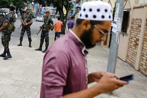 Một người dân sử dụng điện thoại bên cạnh lực lượng an ninh Sri Lanka đứng gác trên đường phố. (Nguồn: ndtv.com)