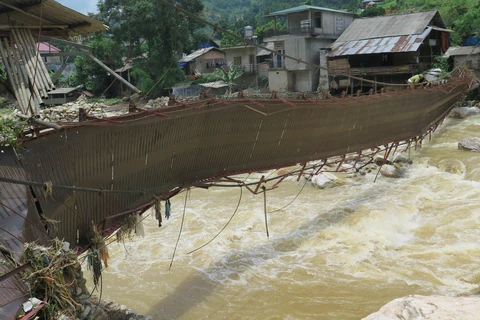 Một số người dân bất chấp nguy hiểm vẫn cố gắng đi qua cây cầu Bản Dền, xã Bản Hồ, huyện Sa Pa đã bị hư hỏng nặng sau trận lũ lớn. (Ảnh: Hương Thu/TTXVN)
