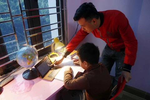 Phụ huynh hỗ trợ học sinh lớp 3 trường Tiểu học Hoàng Lê, thành phố Hưng Yên học trực tuyến tại nhà. (Ảnh: Phạm Kiên/TTXVN)
