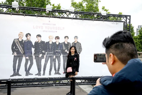 Một phụ nữ chụp ảnh phía trước tấm poster hình ảnh nhóm nhạc BTS bên ngoài sân vận động Stade-de-France, Paris, Pháp. (Nguồn: AFP)