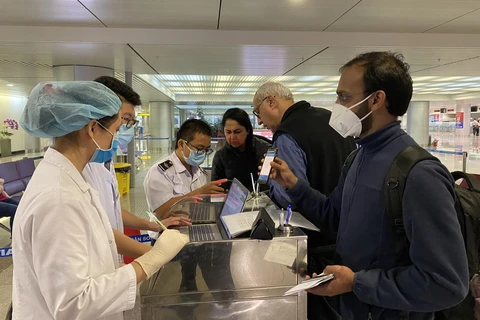 Nhân viên Trung tâm Kiểm dịch y tế quốc tế hướng dẫn hành khách thực hiện tờ khai y tế trước khi làm thủ tục nhập cảnh tại sân bay Tân Sơn Nhất Thành phố Hồ Chí Minh. (Nguồn: TTXVN phát)
