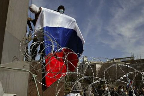 Một người đàn ông đeo mặt nạ cầm cờ Nga tại tòa nhà chính quyền khu vực ở Donetsk. (Nguồn: AP)