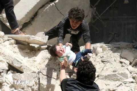 Sơ tán một em bé khỏi đống đổ nát sau các cuộc không kích tại thành phố Aleppo ngày 28/4. (Nguồn: AFP/TTXVN)