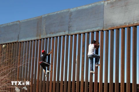Hai cậu bé cố gắng trèo qua bức tường biên giới giữa Mỹ và Mexico tại Ciudad Juarez, Mexico ngày 26/1. (Nguồn: AFP/TTXVN)