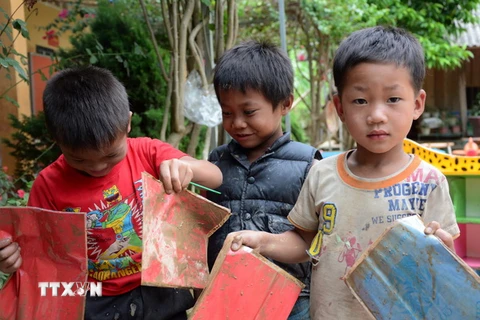 Trẻ em trong xã Mường lói nhặt những tập giấy màu dính đầy bùn đất. (Ảnh: Văn Dũng/TTXVN)