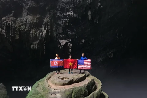 Khách du lịch khám phá hang động chụp ảnh cùng với 3 lá quốc kỳ Mỹ-Triều Tiên-Việt Nam tại hang Én, tỉnh Quảng Bình. (Ảnh: TTXVN phát)