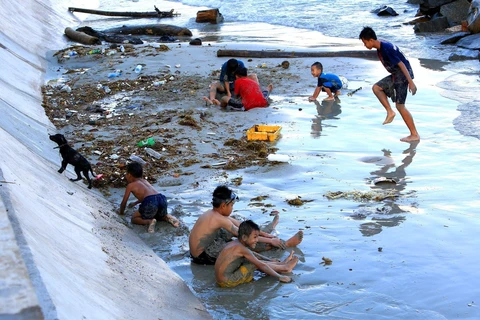 Những đứa trẻ chơi đùa cùng với rác tại bãi tắm gần Cầu Tàu 914. (Ảnh: Ngọc Hà/TTXVN)