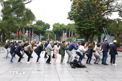 Đoàn khách du lịch quốc tế cùng tập thể dục với người dân Thủ đô tại khu vực vườn hoa Lý Thái Tổ bên hồ Hoàn Kiếm. (Ảnh: Minh Quyết/TTXVN)