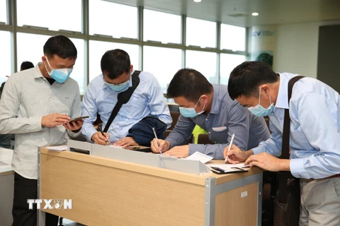 Nhân viên y tế kiểm tra phiếu khai báo y tế của hành khách trước khi làm thủ tục nhập cảnh tại cửa khẩu Sân bay quốc tế Nội Bài (Hà Nội), chiều 7/3. (Ảnh: Dương Giang/TTXVN)
