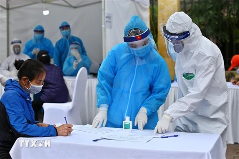 Nhân viên y tế hướng dẫn người dân khai vào tờ khai khi đến test nhanh COVID-19. (Ảnh: Minh Quyết/TTXVN)