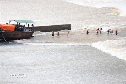 Lực lượng chức năng hỗ trợ những người bị mắc kẹt giữa đập Nam Thạch Hãn di chuyển ra khỏi vùng nguy hiểm, trước khi đưa vào bờ. (Ảnh: Nguyên Lý/TTXVN)