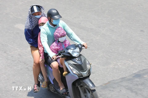 Một gia đình phải mặc áo chống nắng khi phải di chuyển trên đường Giải Phóng lúc 11h40. (Ảnh: Hoàng Hiếu/TTXVN)