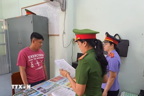 Lực lượng chức năng tống đạt các Quyết định và Lệnh bắt tạm giam đối tượng Phan Thành Được (trái, áo đỏ). (Ảnh: TTXVN phát)