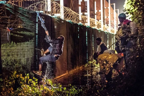 Người di cư trái phép trèo qua hàng rào an ninh để tiến vào đường hầm qua eo biển Manche, do hãng Eurotunnel vận hành, tại Coquelles gần Calais. (Nguồn: AFP).