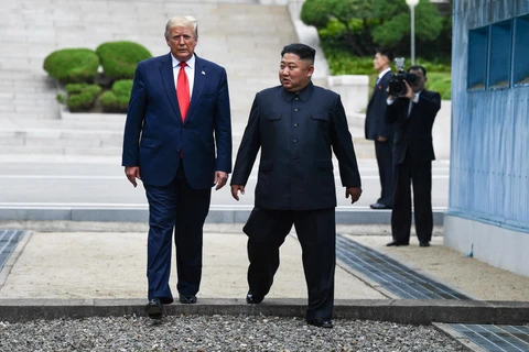 Tổng thống Mỹ Donald Trump (trái) và nhà lãnh đạo Triều Tiên Kim Jong-un bước chân qua đường ranh giới phân chia hai miền Triều Tiên tại DMZ, sang phần lãnh thổ của Triều Tiên. (Ảnh: AFP/TTXVN)