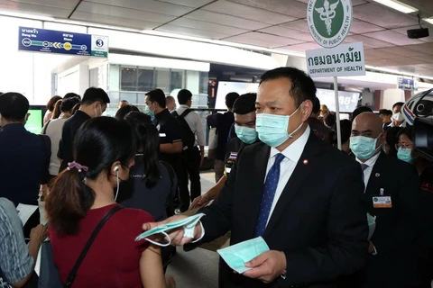 Bộ trưởng Y tế Thái Lan Anutin Charnvirakul (phải) phát khẩu trang cho hành khách tại một nhà ga ở Bangkok. (Ảnh: AFP/TTXVN)