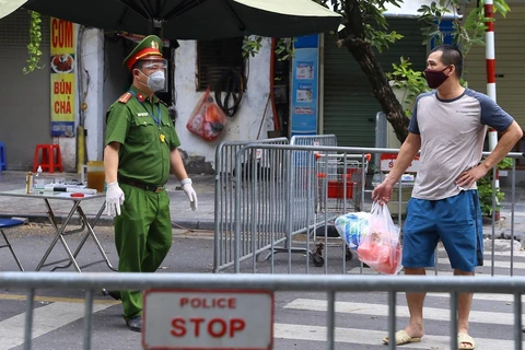 Công an hướng dẫn người dân đưa đồ tiếp tế cho người thân trong Bệnh viện hữu nghị Việt Đức qua cổng đường Tràng Thi. (Ảnh: Hoàng Hiếu/TTXVN)