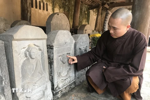 Đại đức Thích Tục Thịnh giảng giải về những hoa văn trên bia đá cổ tại chùa. (Ảnh: Tiến Vĩnh/TTXVN)
